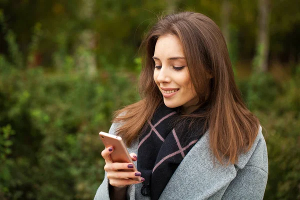 Jonge mooie vrouw in een grijze jas schrijft een bericht — Stockfoto