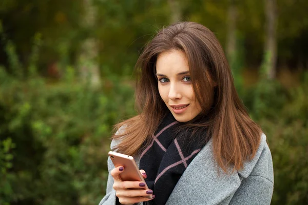 Jonge mooie vrouw in een grijze jas schrijft een bericht — Stockfoto