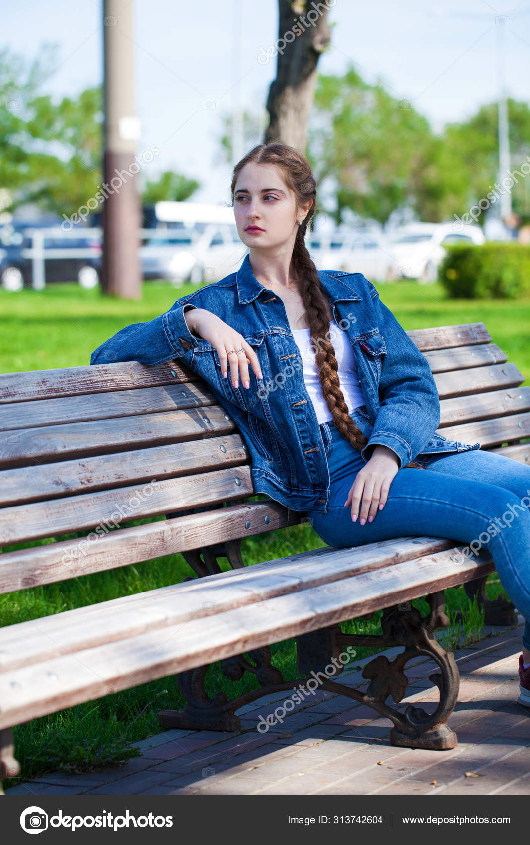 Beautiful Girl In A Denim Jacket Sits On A Bench In A Summer Par