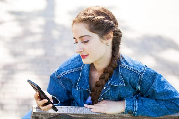 Ung vacker flicka i denim jacka med en telefon i händerna — Stockfoto
