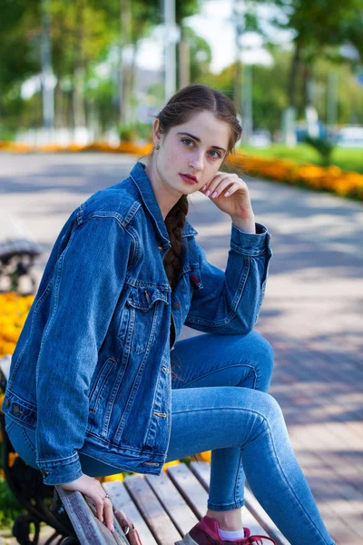 美しいです女の子でデニムジャケットでベンチに座って夏のパー — ストック写真