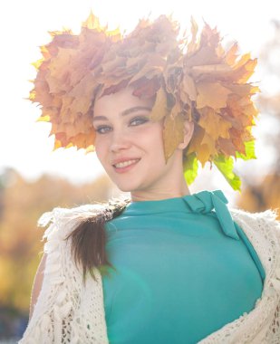 Akçaağaç yapraklarından çelengi olan genç ve güzel bir kadın au pozu veriyor.