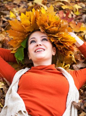 Akçaağaç yapraklarından çelengi olan genç ve güzel bir kadın au pozu veriyor.