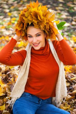 Akçaağaç yapraklarından çelengi olan genç ve güzel bir kadın au pozu veriyor.