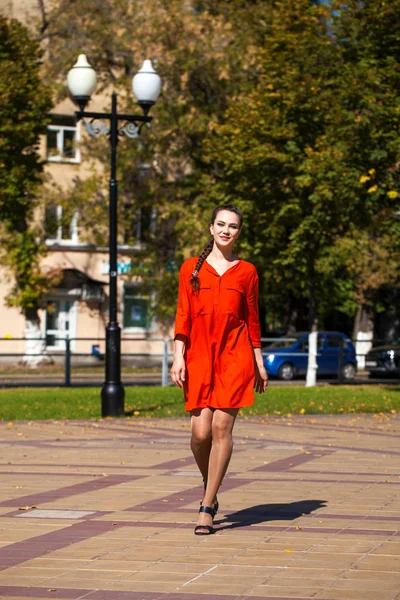 Mladá krásná žena v červených šatech chůze v letní ulici — Stock fotografie