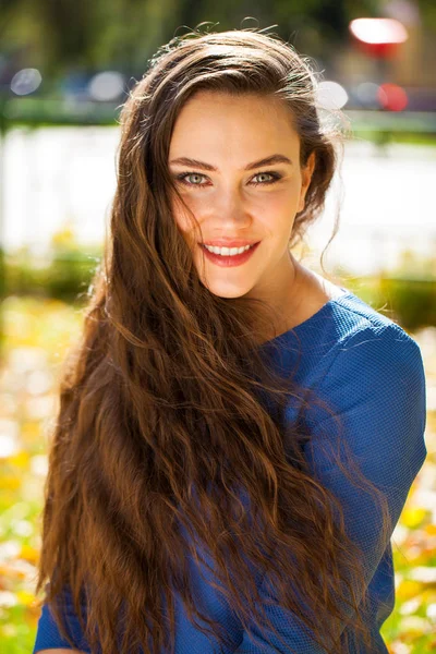 秋の公園で青いドレスを着た若い美しいブルネットの女性 — ストック写真