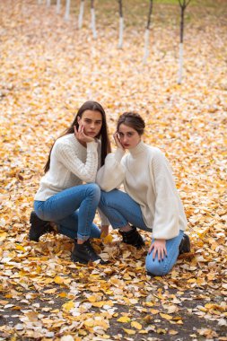 Beyaz yün kazaklı ve kot pantolonlu iki kız arkadaş. 