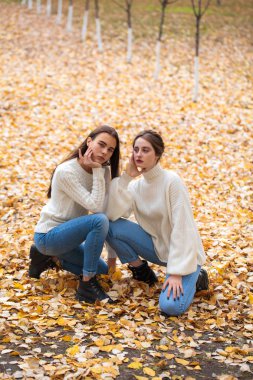 Beyaz yün kazaklı ve kot pantolonlu iki kız arkadaş. 