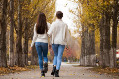 Beyaz yün kazaklı ve kot pantolonlu iki kız arkadaş. 