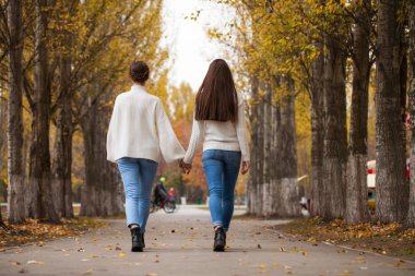 Beyaz yün kazaklı ve kot pantolonlu iki kız arkadaş. 