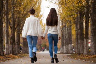 Beyaz yün kazaklı ve kot pantolonlu iki kız arkadaş. 