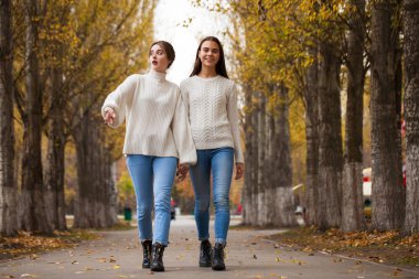 Beyaz yün kazaklı ve kot pantolonlu iki kız arkadaş. 