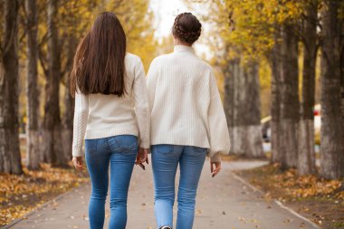 Beyaz yün kazaklı ve kot pantolonlu iki kız arkadaş. 