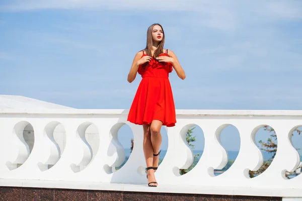 Mladá krásná žena v červených šatech na letní ulici — Stock fotografie