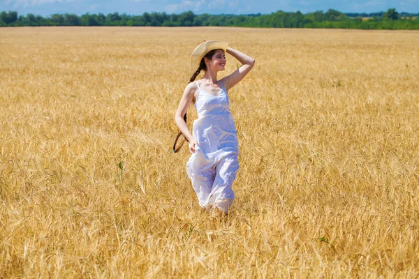 Joven morena vestida de blanco caminando en un campo de trigo — Foto de Stock