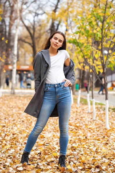 Retrato de una joven hermosa niña en jeans azules y abrigo gris — Foto de Stock