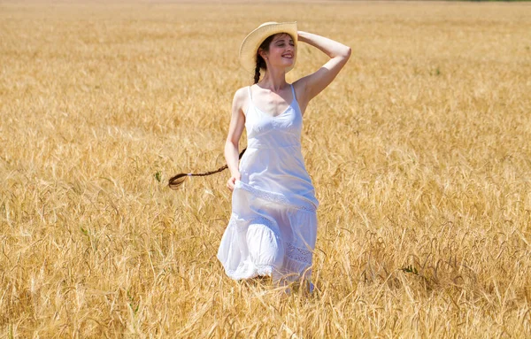 Young brunette woman in white dress walking in a wheat field — Stock Photo, Image