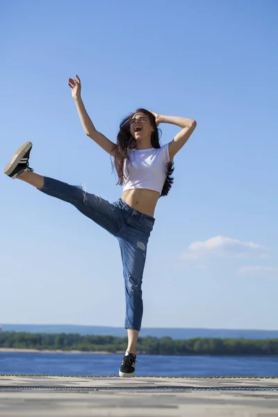 Joven hermosa morena posando contra el cielo azul brillante su —  Fotos de Stock