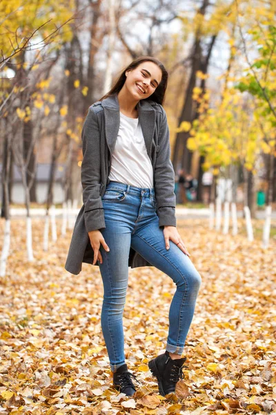 Portret młodej pięknej dziewczyny w niebieskich dżinsach i szarym płaszczu — Zdjęcie stockowe