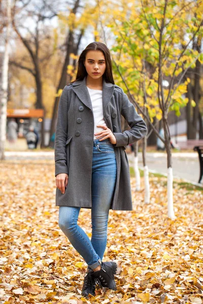 Retrato de una joven hermosa niña en jeans azules y abrigo gris — Foto de Stock