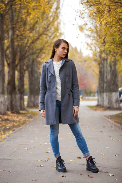 Retrato de una joven hermosa niña en jeans azules y abrigo gris —  Fotos de Stock