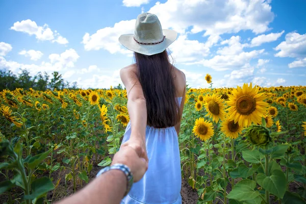 Folge mir, junge Frau hält einem Mann ein Feld mit Sonnenblumen in der Hand — Stockfoto