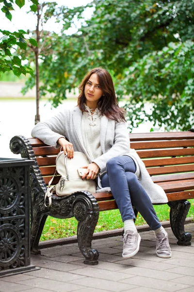 Νεαρή όμορφη γυναίκα που κάθεται σε ένα παγκάκι στο πάρκο φθινόπωρο — Φωτογραφία Αρχείου