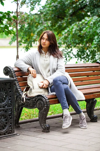 Jeune belle femme assise sur un banc dans le parc d'automne — Photo