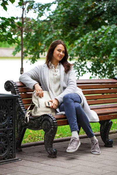 Junge schöne Frau sitzt auf einer Bank im herbstlichen Park — Stockfoto