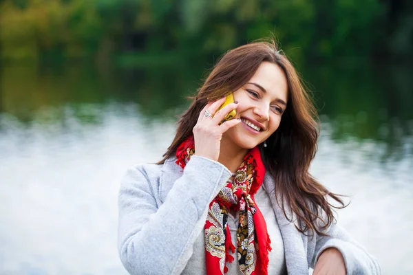 Portrait de heureuse jeune femme brune en manteau beige parlant sur — Photo
