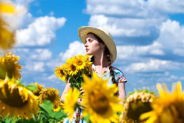 Ung vacker kvinna i en halmhatt i ett fält av solrosor — Stockfoto