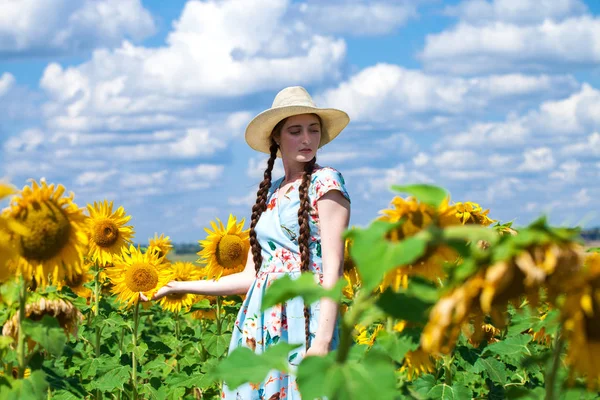 Mulher bonita nova em um chapéu de palha em um campo de girassóis — Fotografia de Stock