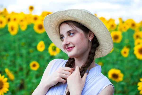 Joven hermosa mujer en un sombrero de paja en un campo de girasoles —  Fotos de Stock