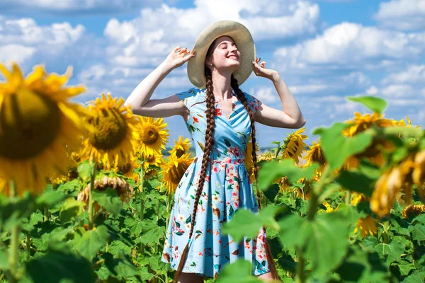 Ung vacker kvinna i en halmhatt i ett fält av solrosor — Stockfoto