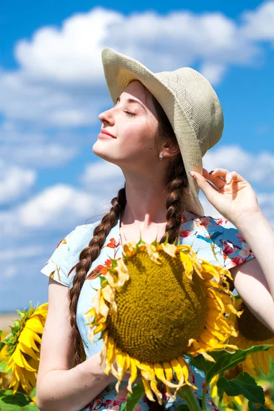 Ung vacker kvinna i en halmhatt i ett fält av solrosor — Stockfoto
