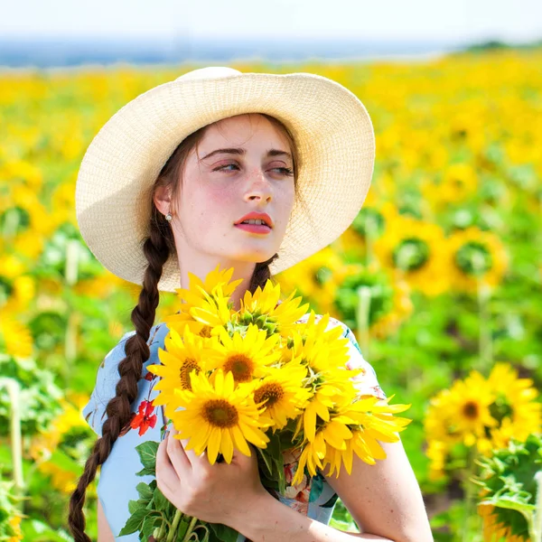 Joven hermosa mujer en un sombrero de paja en un campo de girasoles — Foto de Stock