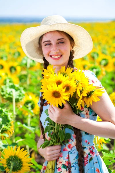 Ung vacker kvinna i en halmhatt i ett fält av solrosor — Stockfoto