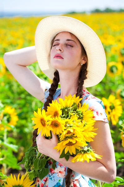 Ung vacker kvinna i en halmhatt i ett fält av solrosor — Stockfoto