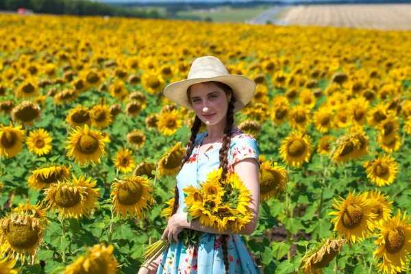 Joven hermosa mujer en un sombrero de paja en un campo de girasoles — Foto de Stock