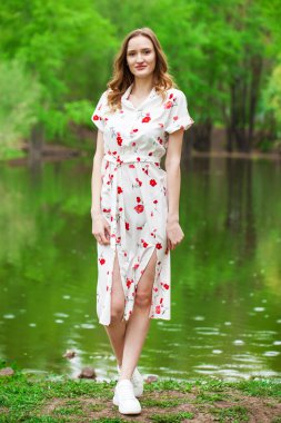 Göl kenarında poz veren beyaz elbiseli güzel bir kadının vücut portresi.