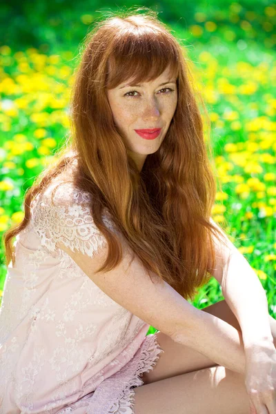 タンポポの牧草地にポーズをとっている若い美しい赤毛の女性の肖像 — ストック写真