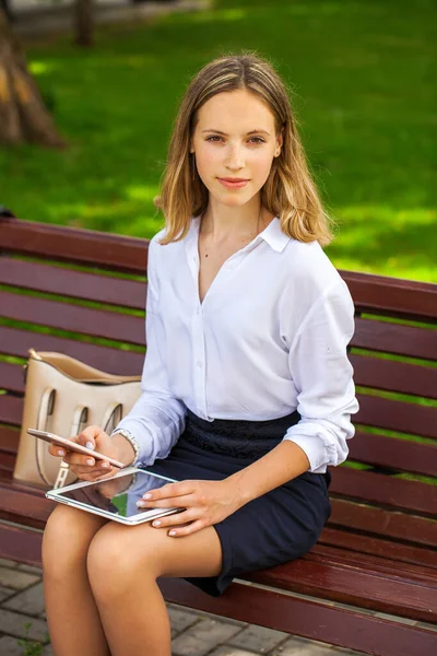 白いシャツのエレガントな成功したビジネスの女の子をブロンドに行くとタッチパッド中に休憩中に屋外に座って夏の公園の背景に — ストック写真
