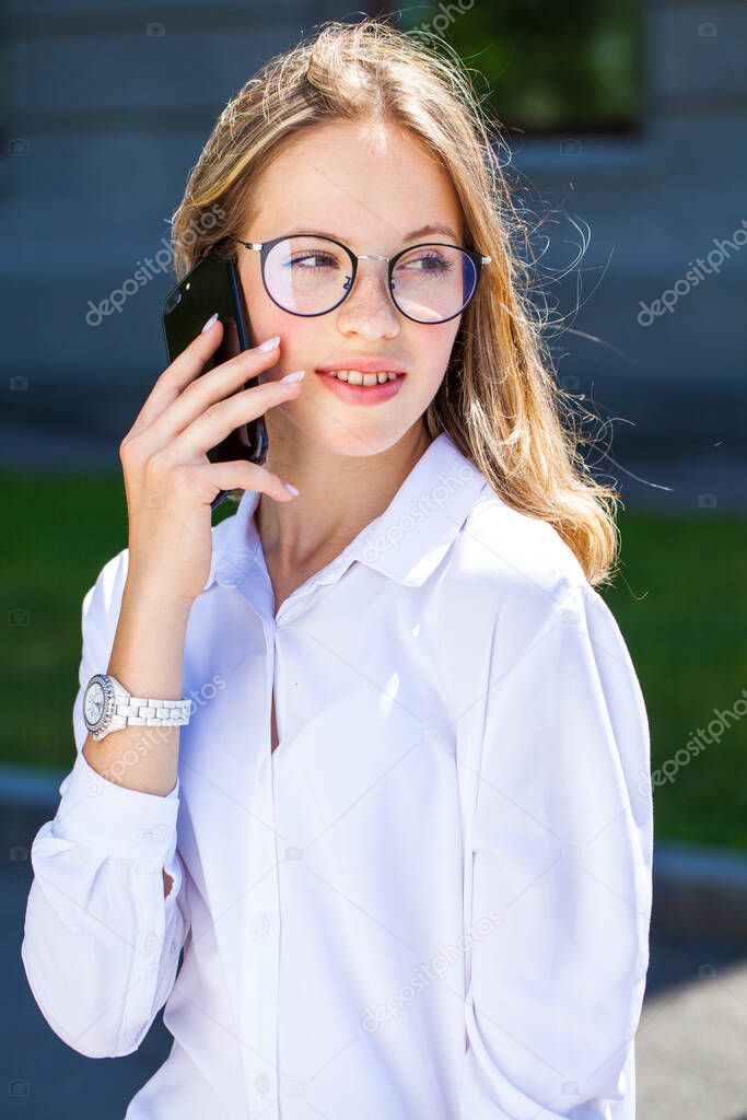 Portrait of a young assistant in a white blouse phoning on the street