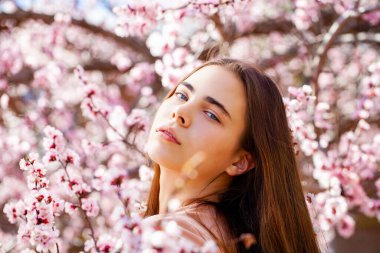 Çiçek açan kiraz ağacının yanında pembe çiçeklerle poz veren güzel kız. Bahar Parkı