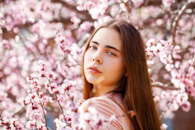 Çiçek açan kiraz ağacının yanında pembe çiçeklerle poz veren güzel kız. Bahar Parkı