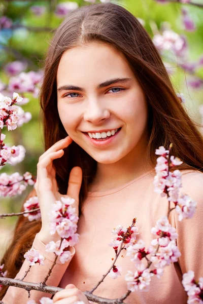 ピンクの花を持つ桜の木の近くにポーズ美少女10代 春の公園 — ストック写真
