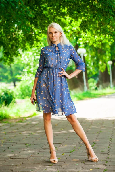 一个穿着蓝色花衣服的金发姑娘在夏日公园里散步的画像 — 图库照片
