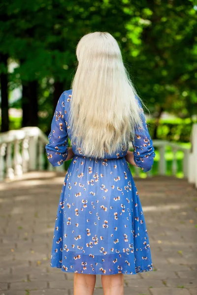 一个穿着蓝色花衣服的金发姑娘在夏日公园里散步的画像 — 图库照片