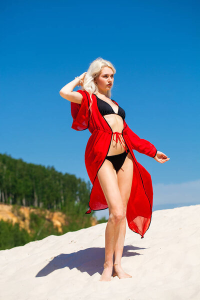 Full body portrait of a young beautiful blonde girl in black bikini and red tunic