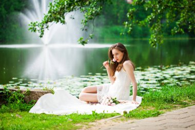 Göl kenarında poz veren beyaz elbiseli güzel bir kadının vücut portresi.